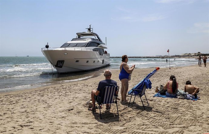 Bañistas en la Playa de Pinedo delante de un yate varado con la bandera de Gran Bretaña, a 5 de junio de 2024, en Valncia