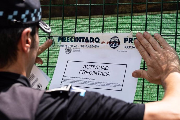 Un policía pega un cartel de actividad precintada donde se está llevando a cabo la obra en el polígono de La Cantueña, a 5 de junio de 2024, en Fuenlabrada, Madrid (España). 