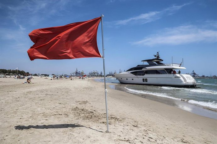 Una bandera roja delante del yate varado en la Playa de Pinedo