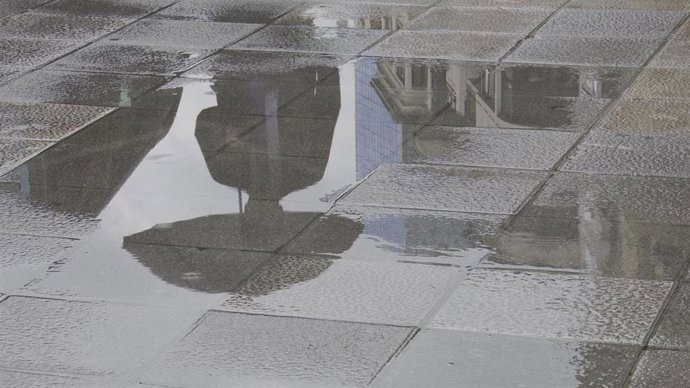 Archivo - Una persona con paraguas se refleja en un charco provocado por la lluvia esta mañana en Bilbao.