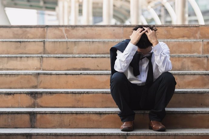 Archivo - Malestar estresado joven hombre de negocios asiático en traje con manos en la cabeza sentado en las escaleras. Concepto de desempleo y despido.