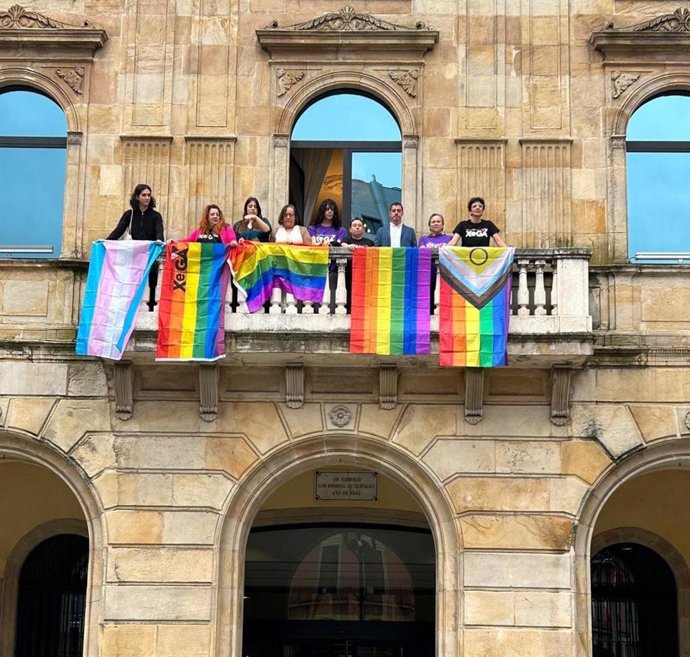 Representantes de los grupos municipales de Gijón de PSOE, IU - Más País - IAS y Podemos y representantes de Xega, en el Balcón Municipal del Ayuntamiento gijonés, con banderas representantivas del colectivo LGTBI.