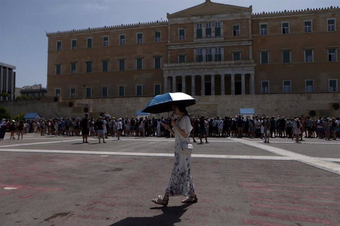 Una persona pasea bajo un paraguas en la plaza Sintagma de Atenas, con el Parlamento al fondo