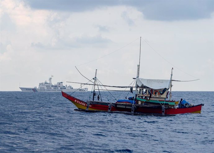 Archivo - Un barco pesquero filipino (frente) y un buque de la Guardia Costera de China (fondo) en el mar de China Meridional