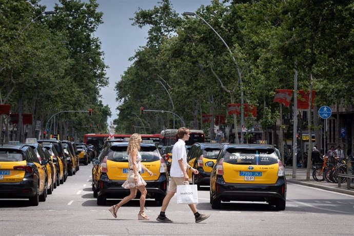 Varias personas cruzan un paso de cebra por Gran Via de Les Corts Catalanes durante una marcha lenta de taxis convocada por Élite Taxi, a 28 de mayo de 2024, en Barcelona, Catalunya (España).