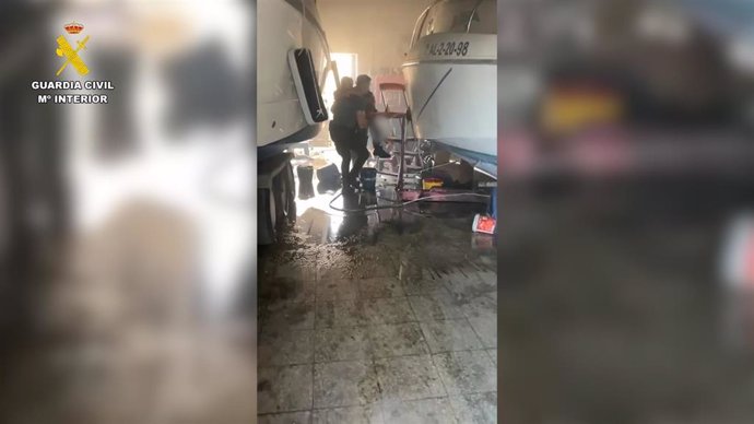 Momento en que los guardias civiles trasladan al herido en la nave incendiada en Chipiona.