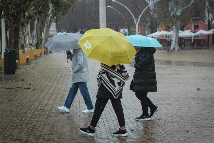 Archivo - Tres personas se protegen de la lluvia con paraguas.