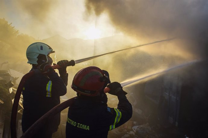 June 19, 2024, Koropi, Eastern Attica, Greece: Firefighters attempt to extinguish a fire amidst thick smoke that has broke out in a factory area during a wildfire in the eastern suburbs of the Greek capital. Authorities have urged residents to evacuate an