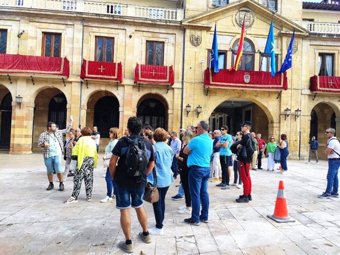 Archivo - Un grupo de turistas escucha las explicaciones de un guía en la Plaza de la Constitución, con el Ayuntamiento de Oviedo al fondo.