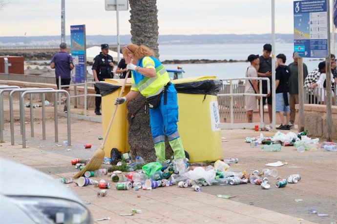 Una trabajadora de Emaya recogiendo residuos en el suelo, junto a unos contenedores, en el paseo junto a la playa, tras la noche de San Juan.