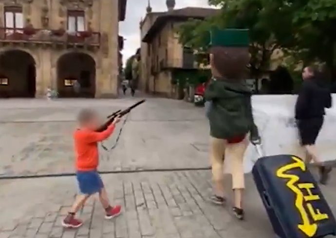 Niño apuntando con un rifle de juguete a un cabezudo de la Guardia Civil