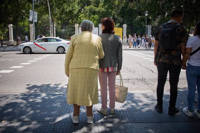 Archivo - Una mujer mayor espera para cruzar una calle, con ayuda, por el centro de la ciudad,
