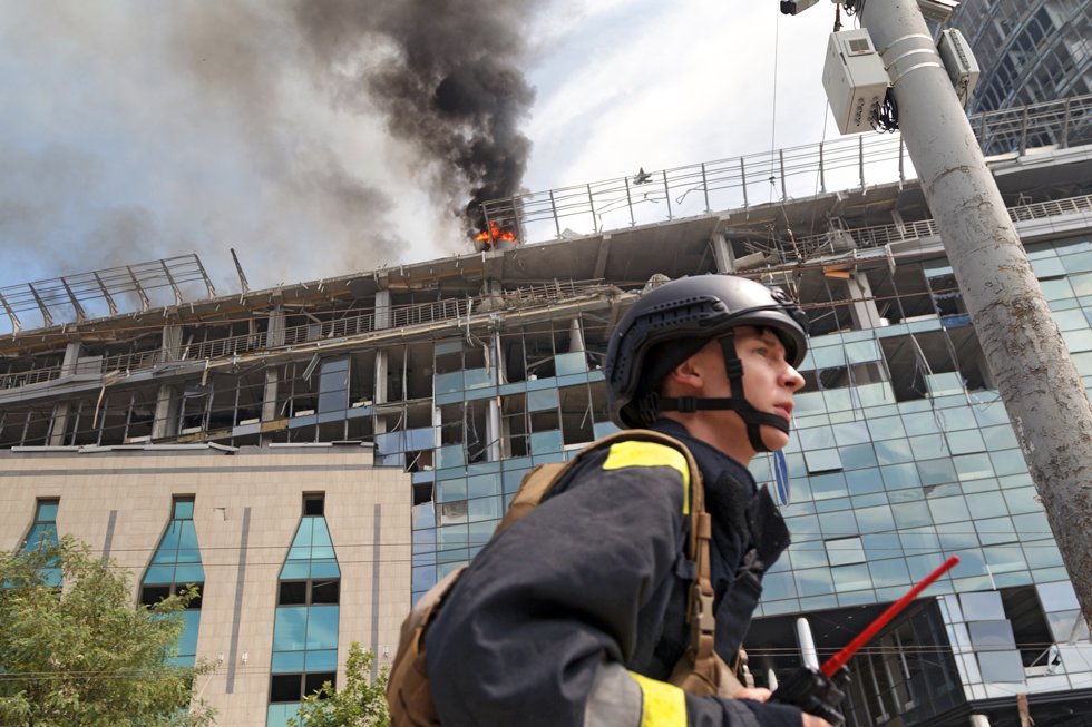 08 July 2024, Ukraine, Kyiv: A rescue worker walks past as a pillar of smoke rises from the burning roof of an unfinished building near the Lukianivska metro station as a result of a Russian missile attack on Kyiv, capital of Ukraine.