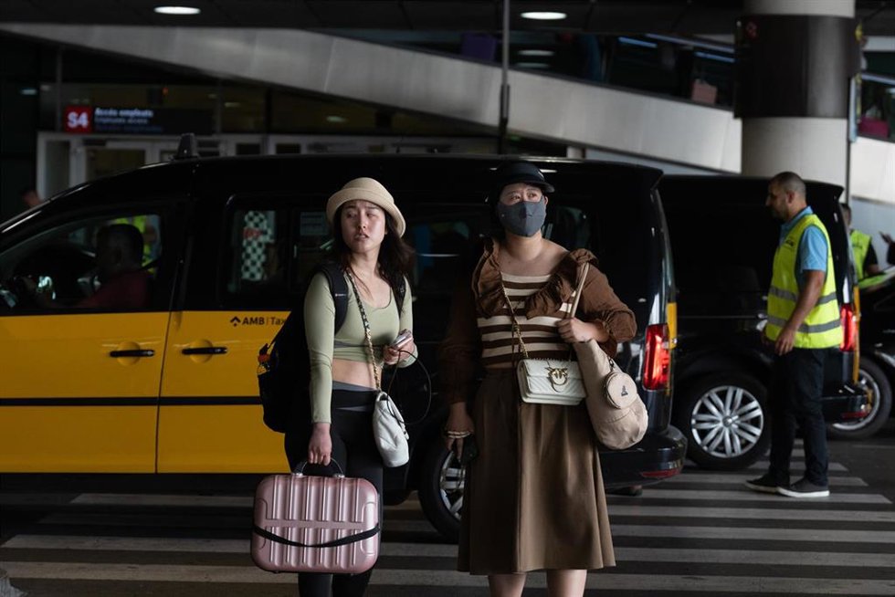 Turistas en el aeropuerto de Barcelona con la concentración de taxistas al fondo