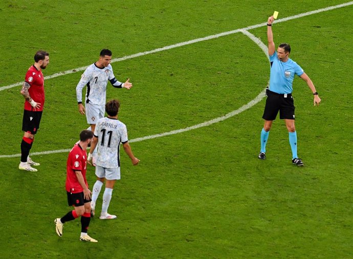 26 June 2024, North Rhine-Westphalia, Gelsenkirchen: Portugal's Cristiano Ronaldo (C) receives a yellow card from referee Sandro Scharer (R) for complaining during the UEFA Euro 2024 Group F soccer match between Georgia and Portugal at Arena auf Schalke. 