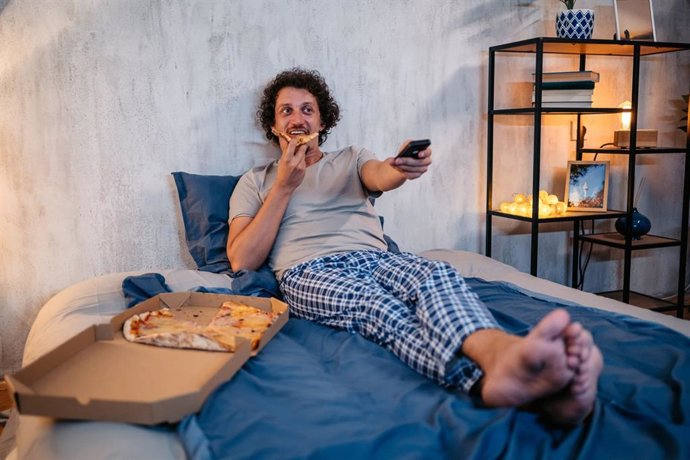 Archivo - Hombre cenando pizza en la cama.