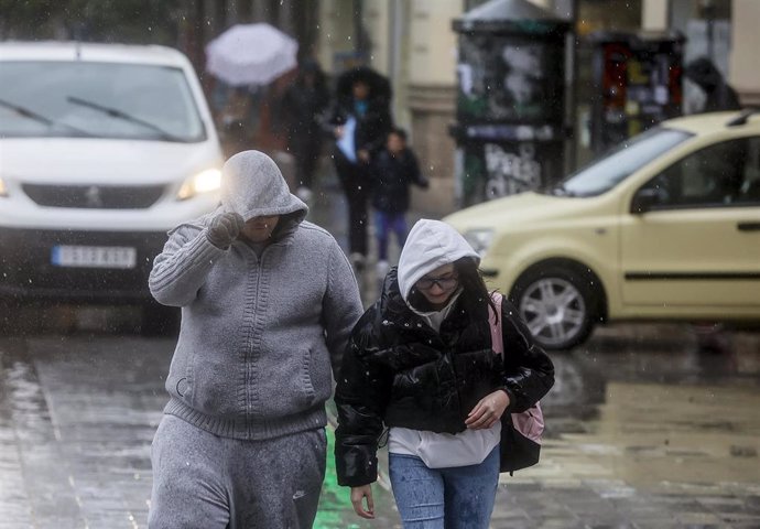 Archivo - Dos personas se tapan la cabeza con la capucha de la chaqueta como consecuencia de la lluvia en imagen de archivo
