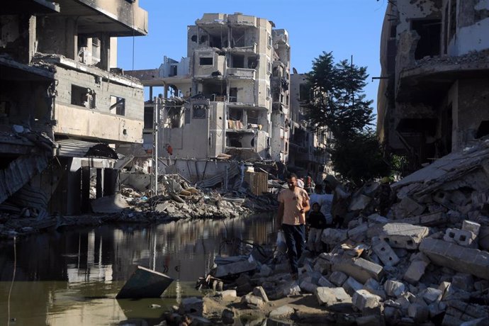 Palestinos caminan entre aguas residuales y edificios destruidos por la ofensiva del Ejército de Israel contra la ciudad de Jan Yunis, en el sur de la Franja de Gaza (archivo)
