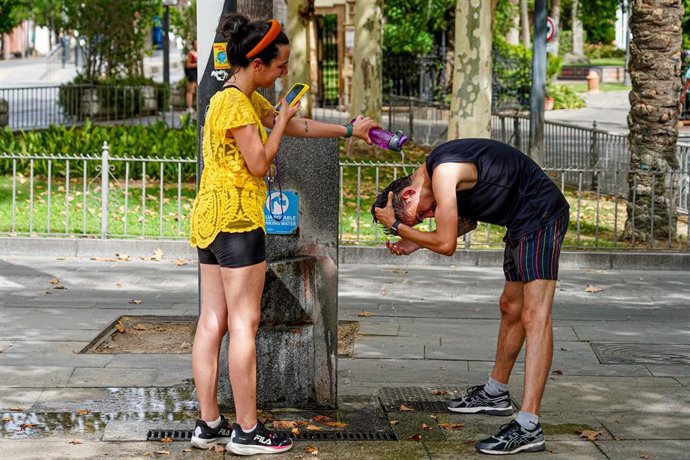 Archivo - Una joven turista le hace una foto a un joven mientras le está refrescando la cabeza.