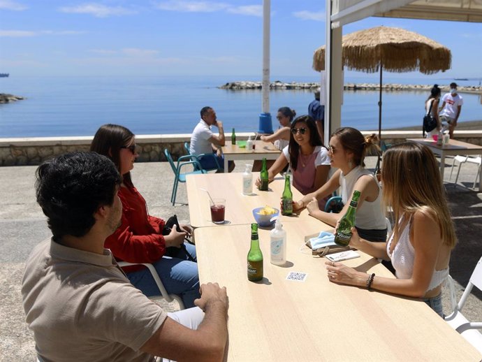 Varias personas disfrutan de la terraza de un bar en el paseo marítimo en Málaga.