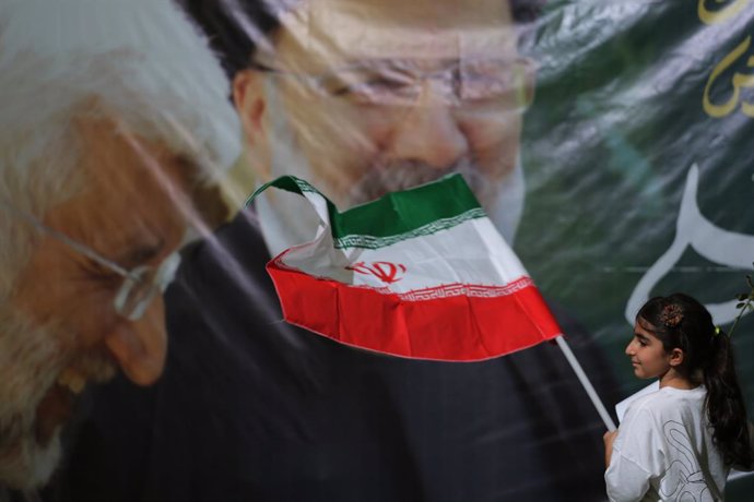 July 3, 2024, Tehran, Iran: An Iranian child girl waves an Iran's flag in front of a large poster of the late president Ebrahim Raisi (R) and Iranian ultraconservative former nuclear negotiator Saeed Jalili (L) during Jalili's election campaign, two days 