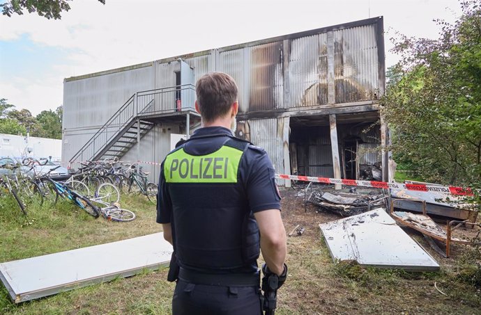 08 July 2024, Lower Saxony, Buchholz: A police officer stands in front of the wall sections lying in front of the accommodation containers after an explosion in a refugee shelter. There is an explosion in a refugee shelter in Buchholz in der Nordheide. Th