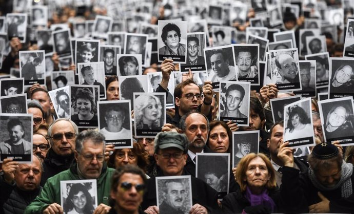 Archivo - FILED - 29 March 2017, Argentina, Buenos Aires: People hold up pictures of victims at a commemoration ceremony 23 years after the terrorist attack on the Jewish community AMIA in Buenos Aires, which killed 85 people. 