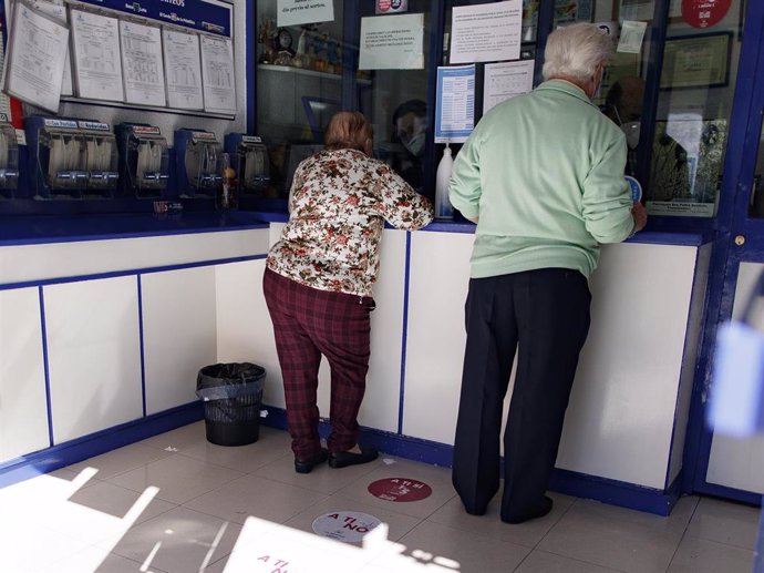 Archivo - Un hombre y una mujer protegidos compran lotería en una Administración 