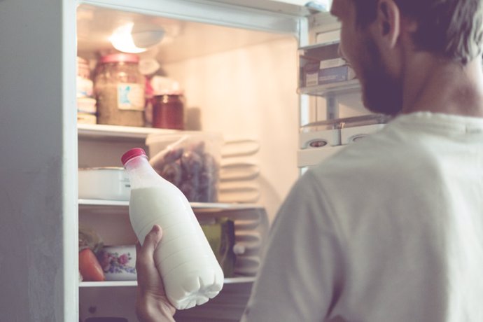 Archivo - Hombre con botella de leche en la mano, nevera abierta