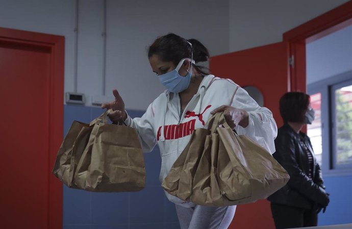 Archivo - Una mujer con bolsas de menú tras ser atendida por una trabajadora de la Fundación Don Bosco, recibe alimentos del Proyecto Fraternitas, que atiende a familias vulnerables de dos de los barrios más pobres 