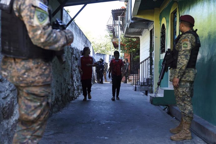 Archivo - December 24, 2022, San Salvador, El Salvador: Kids walk through a passage as soldiers stand guard..Police and military perform a siege in the Tutunichapa Community, a historical point for drug trafficking in the Salvadoran capital, as part of th