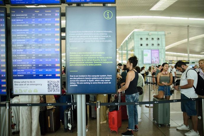 Colas de pasajeros junto a una pantalla que avisa de los problemas causados por la incedencia informática en el Aeropuerto de Barcelona-El Prat.