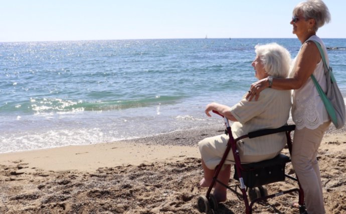 Mayores de vacaciones. Persona mayor en la playa acompañada por un voluntario