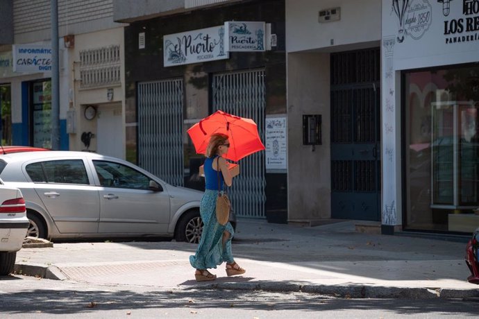 Una persona camina por la calle bajo un paraguas para protegerse del sol. Imagen de archivo