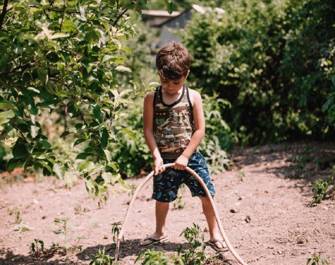 Niño riega un árbol con una manguera.