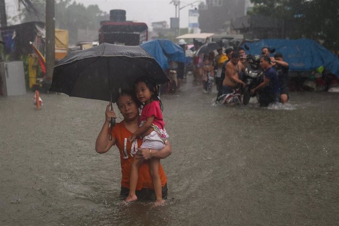 Un grupo de personas intenta avanzar por una calle inundada por las lluvias del monzón en la capital de Filipinas, Manila