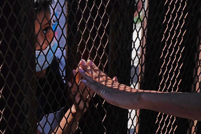 Archivo - 30 April 2021, US, Nogales: A supporter touches the hand of a young asylum-seeking migrant from behind the fence at border wall separating the United States and Mexico. 