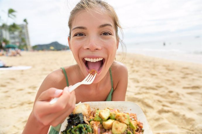 Archivo - Mujer comiendo comida saludable en un tupper en la playa.