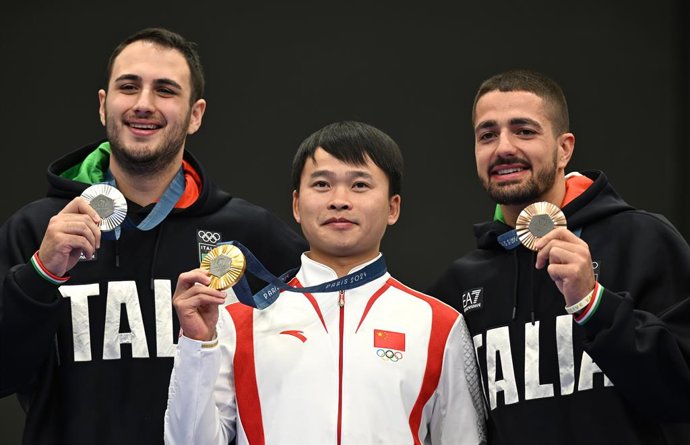 28 July 2024, France, Chateauroux: (L-R) Silver medallist Italy's Federico Nilo Maldini, Gold medallist China's Xie Yu and Bronze medallist Italy's Paolo Monna celebrate on the podium after the shooting 10m air pistol men's final during the Paris 2024 O