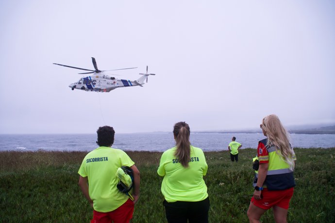 Varios socorristas observan a un helicóptero rescatando a un varón joven en la Punta do Castro, a 28 de julio de 2024, en San Pedro de Benquerencia, Barreiros, Lugo, Galicia (España).