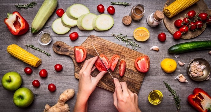 Archivo - Mano femenina corta tomates en una mesa de cocina rústica, concepto vegetariano.