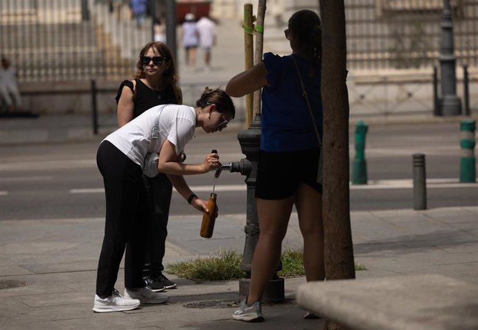 Una mujer rellena una cantimplora en una fuente.