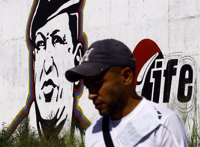 Archivo - Un venezolano delante de una imagen mural de Hugo Chávez