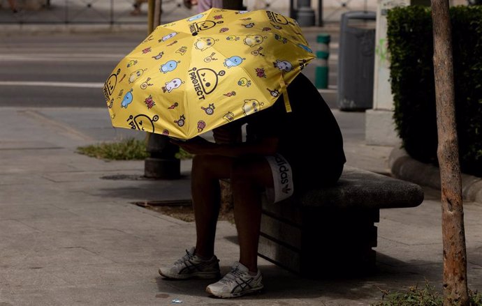 Un hombre se resguarda del sol bajo un paraguas