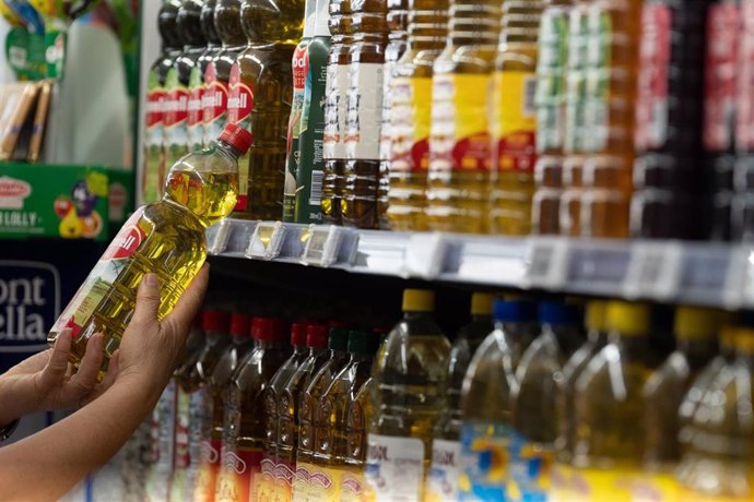 Archivo - Una persona coge una botella de aceite en un supermercado