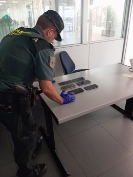 Un agente de la Guardia Civil con algunos de los móviles incautados a los detenidos.