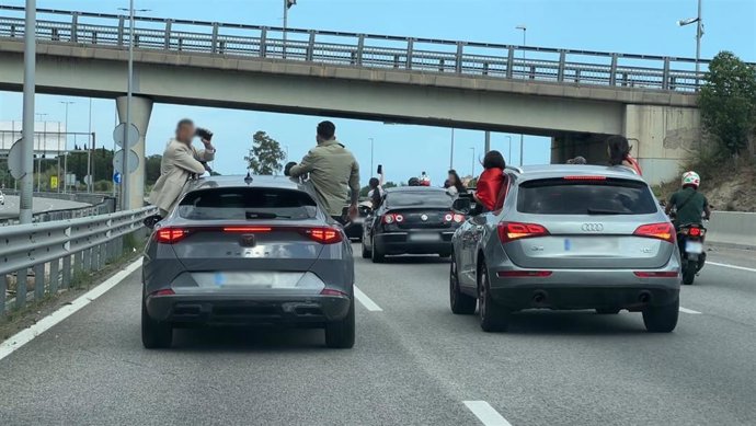 Jóvenes sentados en las ventanas de varios vehículos mientras circulan por la C-32