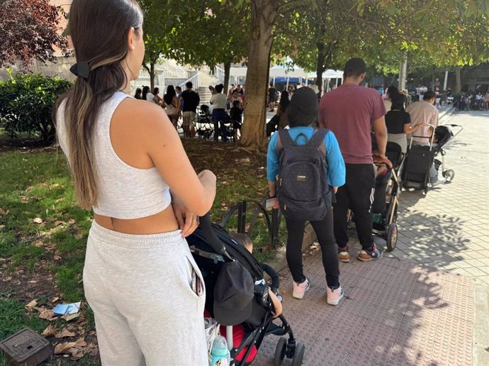 Una mujer con un carrito de bebé hace cola para recibir alimentos.