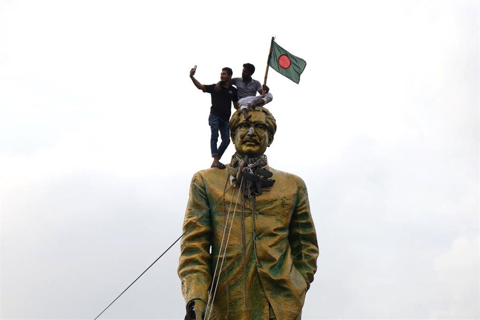 Dos manifestantes se fotografían sobre la estatuta del ex primer ministro Sheij Mujiban Rahman, padre de la también ex primera ministra Sheij Hasina.