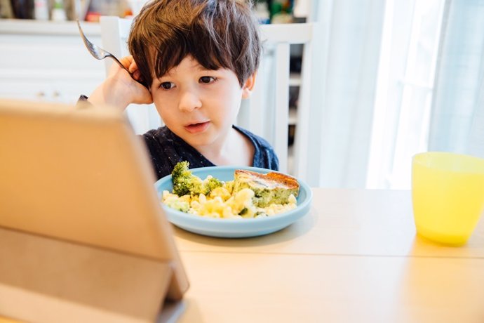 Archivo - NIño comiendo con la tablet